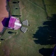 Outdoor wedding setup with chairs and an arch by a pond, and a grassy field, viewed from above
