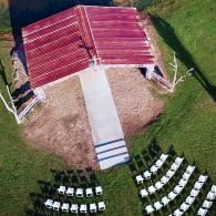 Aerial view of an outdoor pavilion with red roof and rows of white chairs on grass