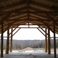 Open-air pavilion with wooden beams overlooking a rustic landscape and distant hills