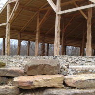 Stone steps leading to a wooden pavilion with open beams and bare trees in the background
