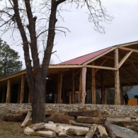 Rustic wooden pavilion with a red roof behind a stone wall and leafless trees