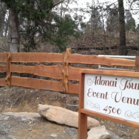 Wooden fence and sign for Adonai Event Venue in a wooded outdoor setting