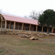 Stone building with a red roof beside trees and rocks in a grassy yard