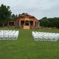 Outdoor wedding setup with white chairs on a green lawn facing a wooden pavilion