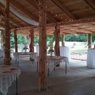 Open-air pavilion with wooden pillars and white-draped tables overlooking a grassy yard