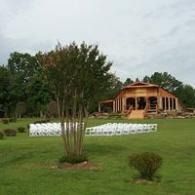 Outdoor wedding setup on a grassy lawn with white chairs and a rustic pavilion under cloudy skies