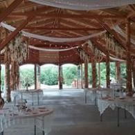 Open-air event pavilion with white-draped tables and wooden beams, overlooking greenery.