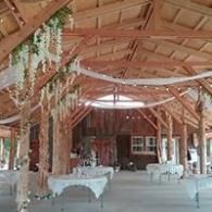 Rustic barn-style hall with wooden beams, draped fabric, and tables set for an event.