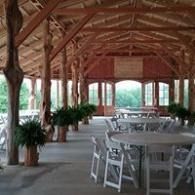 Rustic open-air pavilion with white tables and chairs and potted plants along wooden beams