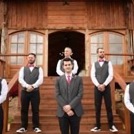 Five men in vests and ties standing on wooden steps in front of a rustic cabin.
