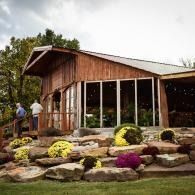 Rustic wooden building with large windows, stone landscaping, and blooming flowers in front
