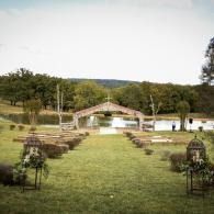Outdoor wedding setup with aisle chairs facing a gazebo and pond in a grassy garden setting