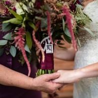 Hands clasped at a wedding ceremony with bouquet and white dress visible