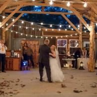 Bride and groom dancing under string lights in a rustic barn wedding venue