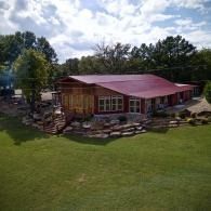 Rustic cabin with a red roof and stone landscaping on a green lawn under a cloudy sky