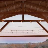 Wooden pavilion roof framing string lights over a distant autumn landscape at dusk