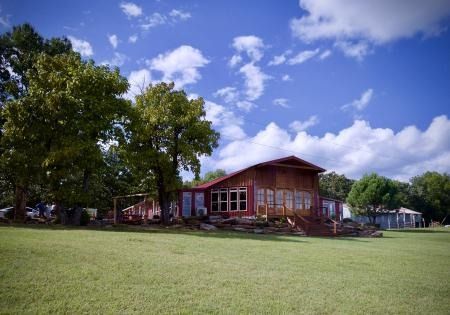 Wooden cabin on a grassy lawn under large trees and a bright blue sky