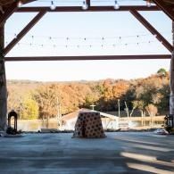 Covered outdoor pavilion overlooking a wooded valley, with a fire pit and string lights overhead