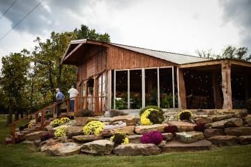 Rustic wooden lodge with stone landscaping and flowering shrubs, people standing by the entrance