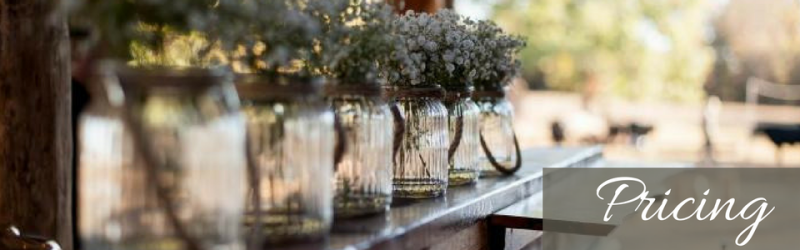Glass jars with floral arrangements on a table, with blurred foreground jars and text that reads “Pricing”