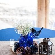 Blue vase with white flowers, pinecones, and a lantern on a table by a window