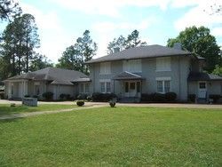 Two-story gray house with a large lawn and trees under a blue sky