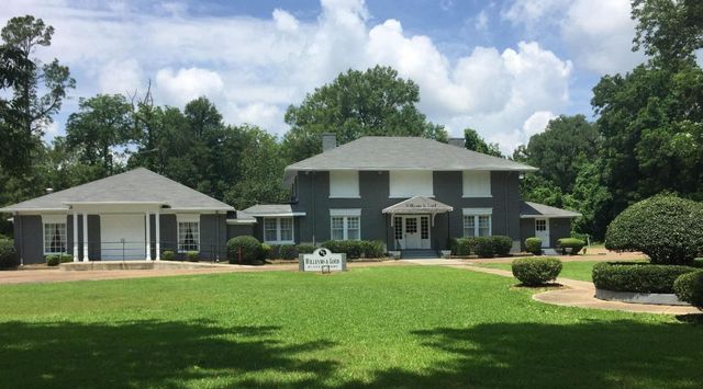 Large gray house with white trim, a carport, and a wide green lawn under a partly cloudy sky