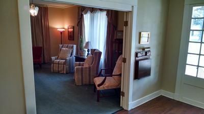 Cozy sitting room with striped armchairs, a lamp, curtains, and a doorway to an adjoining room