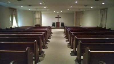 Empty church sanctuary with wooden pews facing a central aisle and a cross at the front.