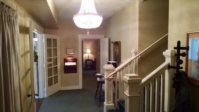 Dim hallway with staircase, chandelier, French doors, and a small table at the far end.