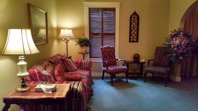 Cozy living room with striped sofa, two chairs, lamps, window, and floral curtains in warm light