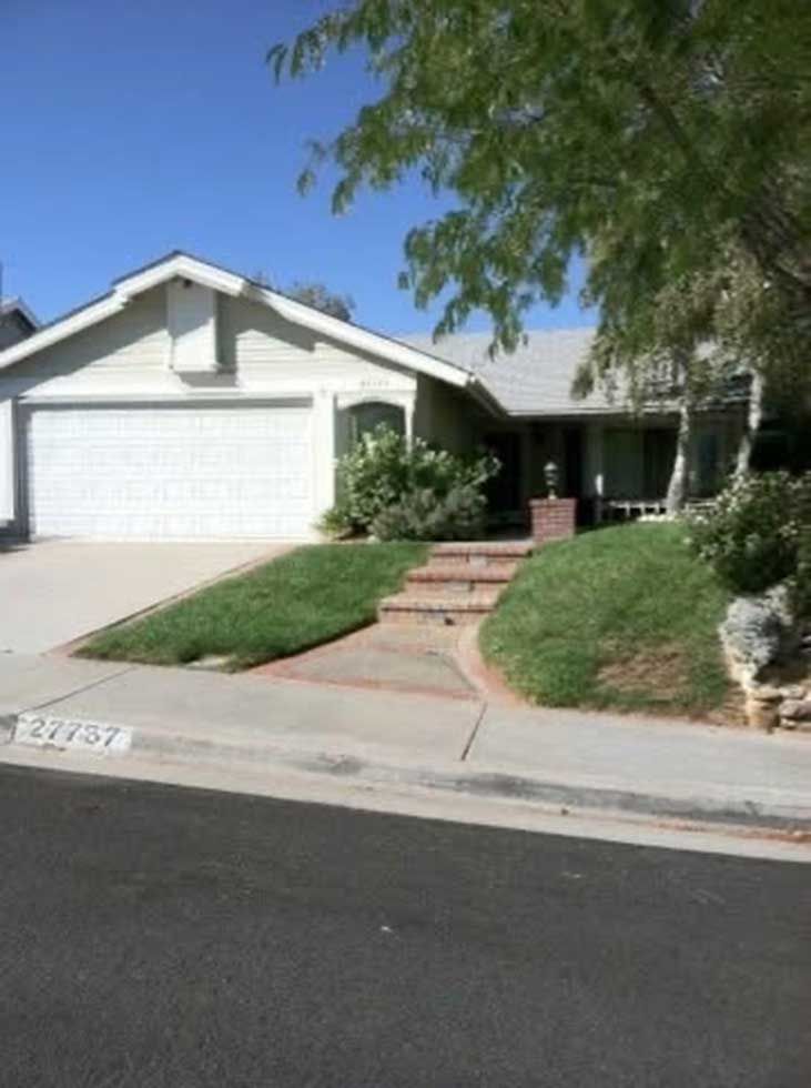Suburban house with white garage, front steps, and desert landscaping along a quiet street.