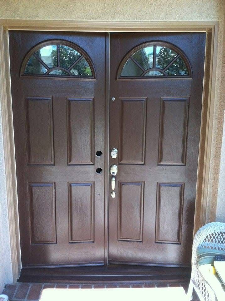Double wooden front doors with arched glass windows in a beige exterior wall