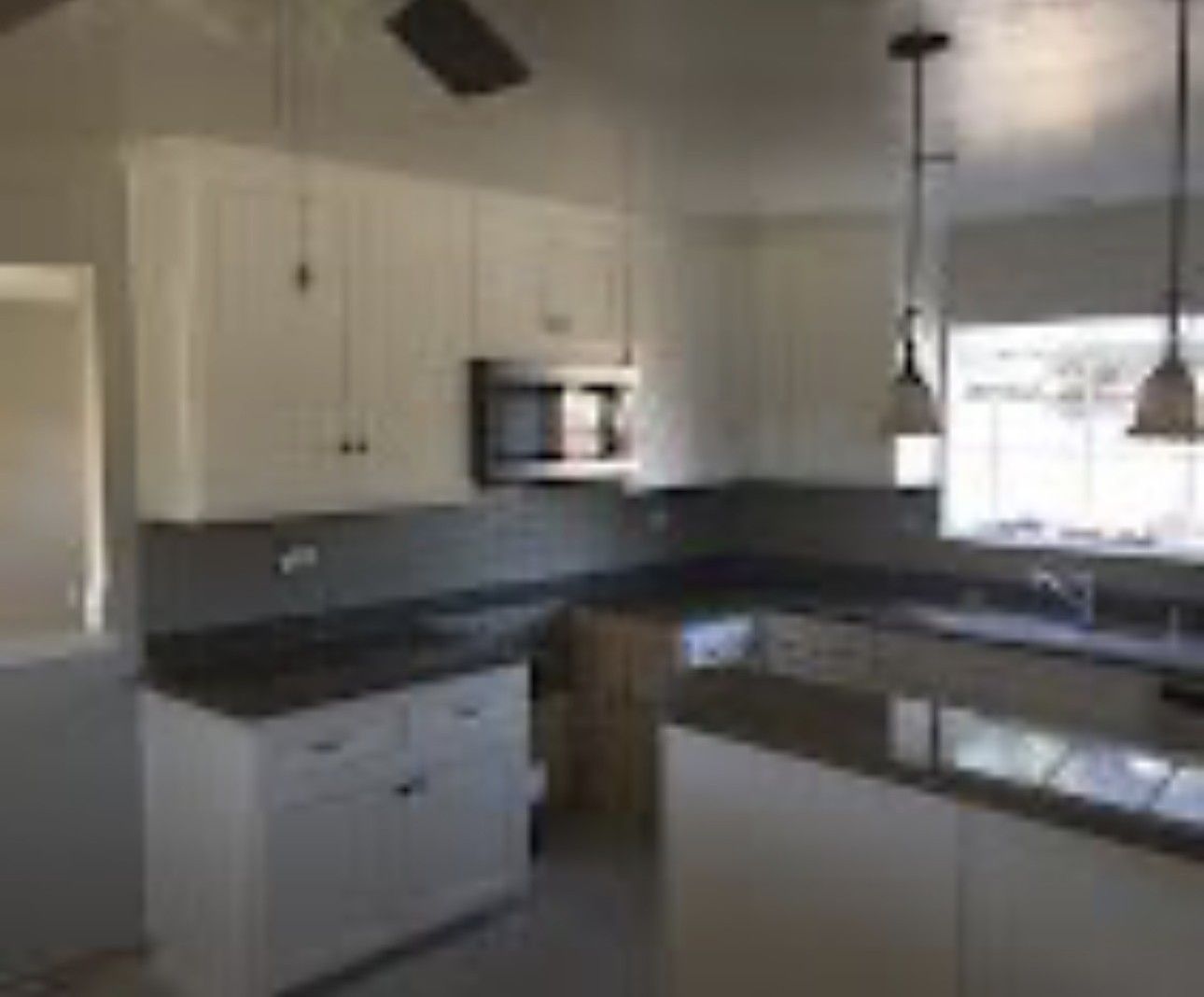 Modern kitchen with white cabinets, dark countertops, stainless appliances, and a window over the sink