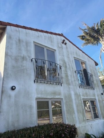 Two-story white stucco house with balconies and windows under a blue sky