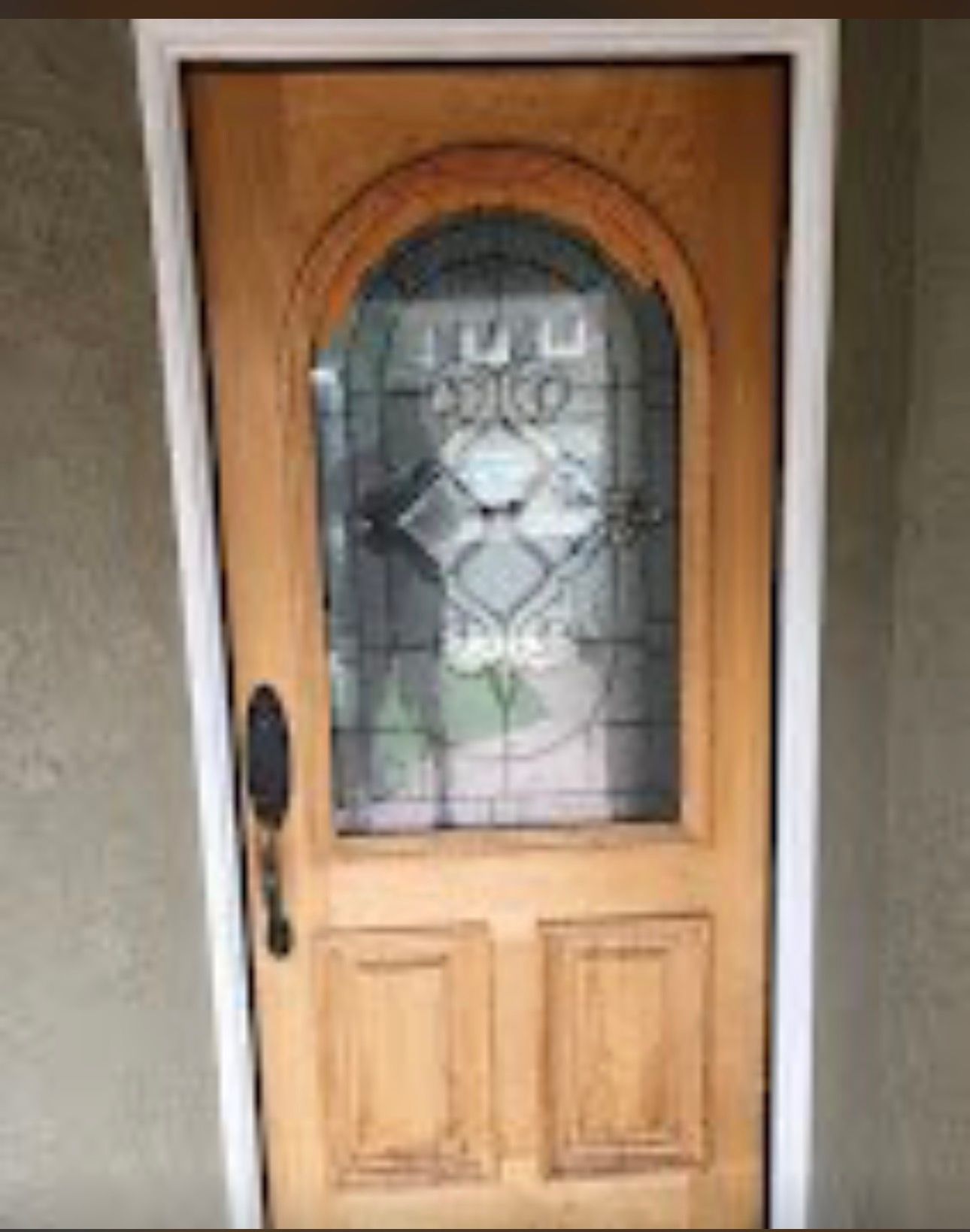 Wooden front door with an arched frosted glass window and black handle on a beige wall