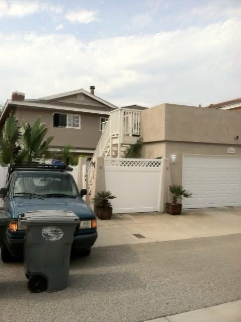 Suburban driveway with a green SUV, trash bin, garage, and beige house under cloudy sky