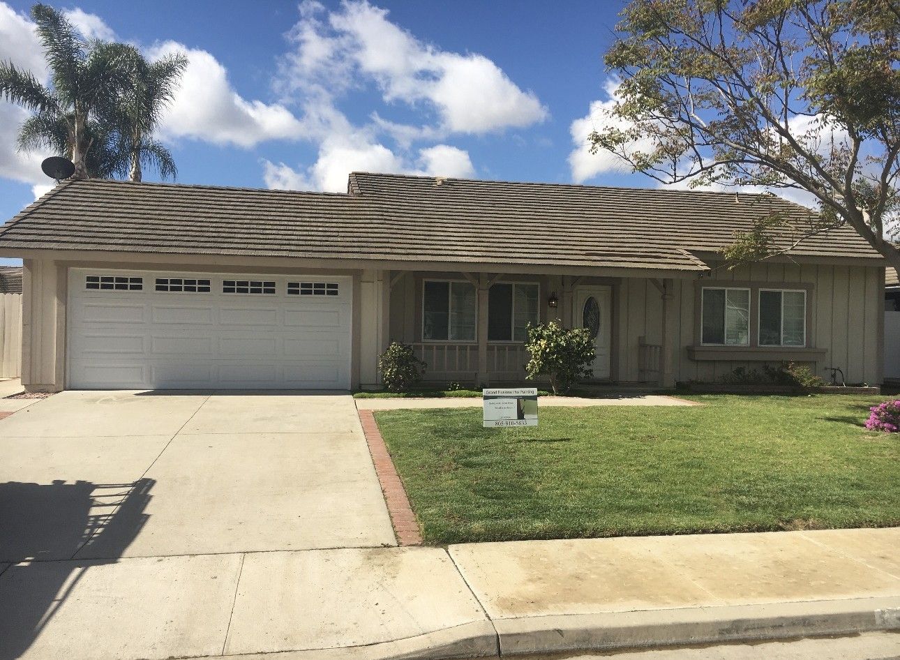 Single-story suburban house with a two-car garage, driveway, and front lawn under a blue sky