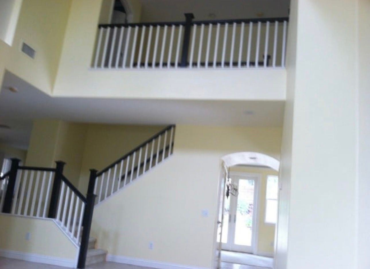 Interior view of a two-story foyer with beige walls, white railings, and a front door visible below