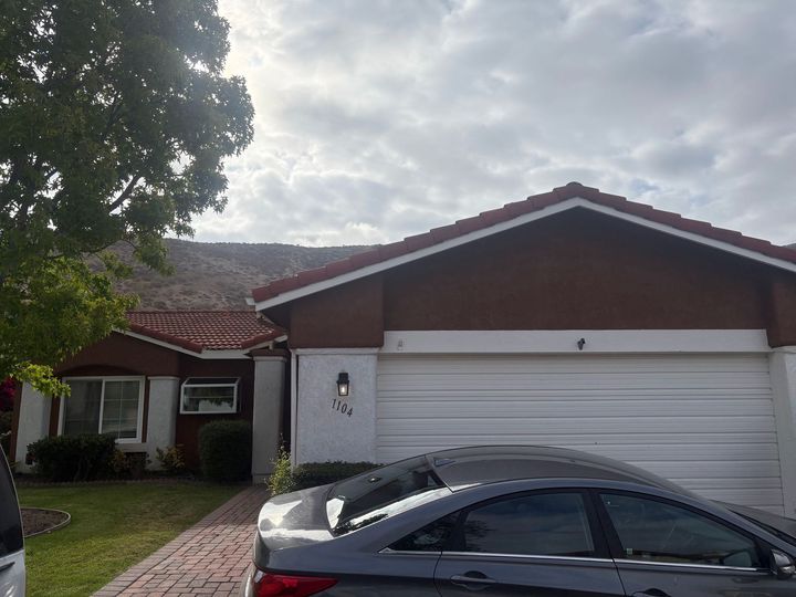 Suburban house with white garage, dark sedan in driveway, and cloudy sky overhead