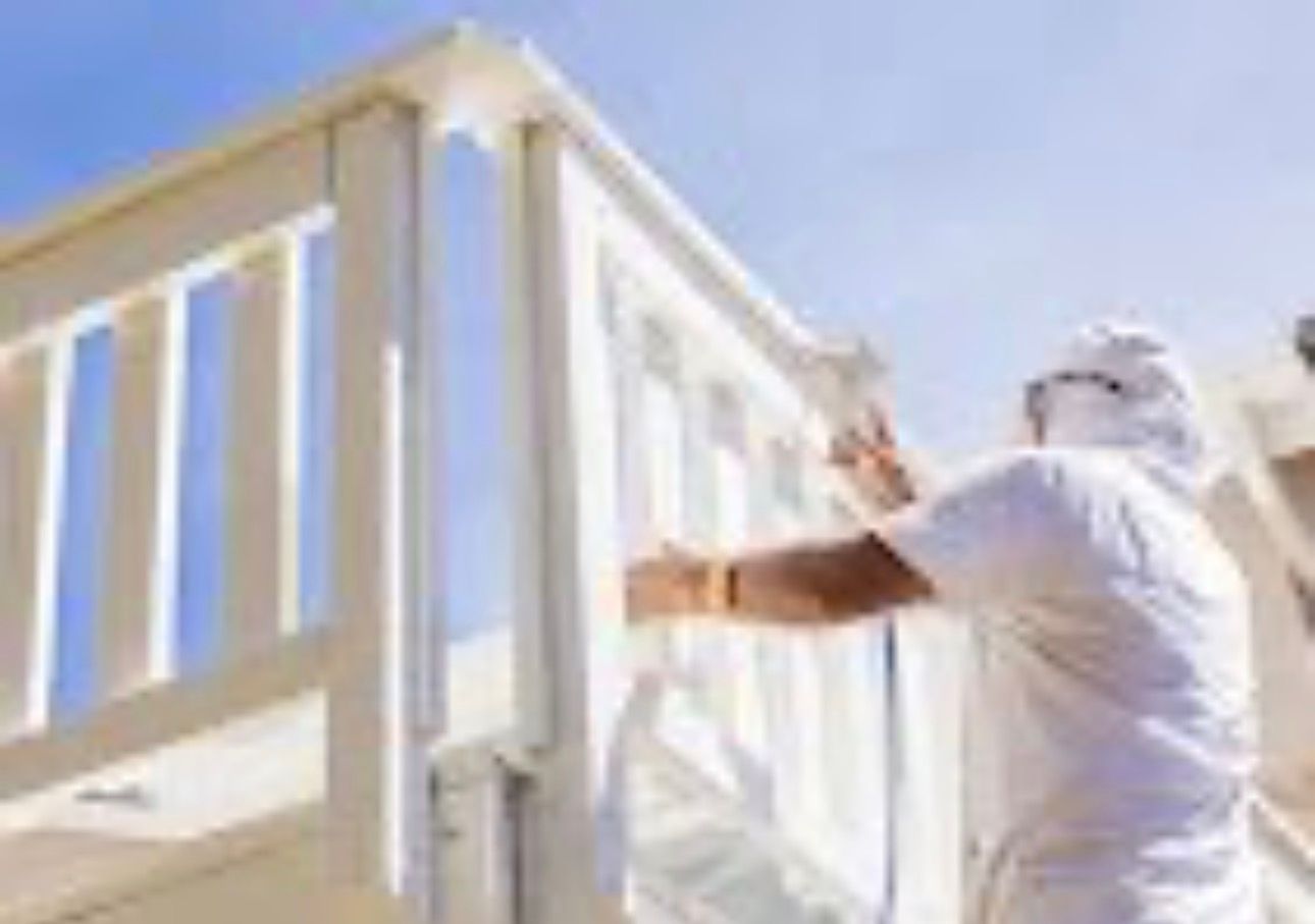 Worker painting a white deck railing outdoors against a blue sky