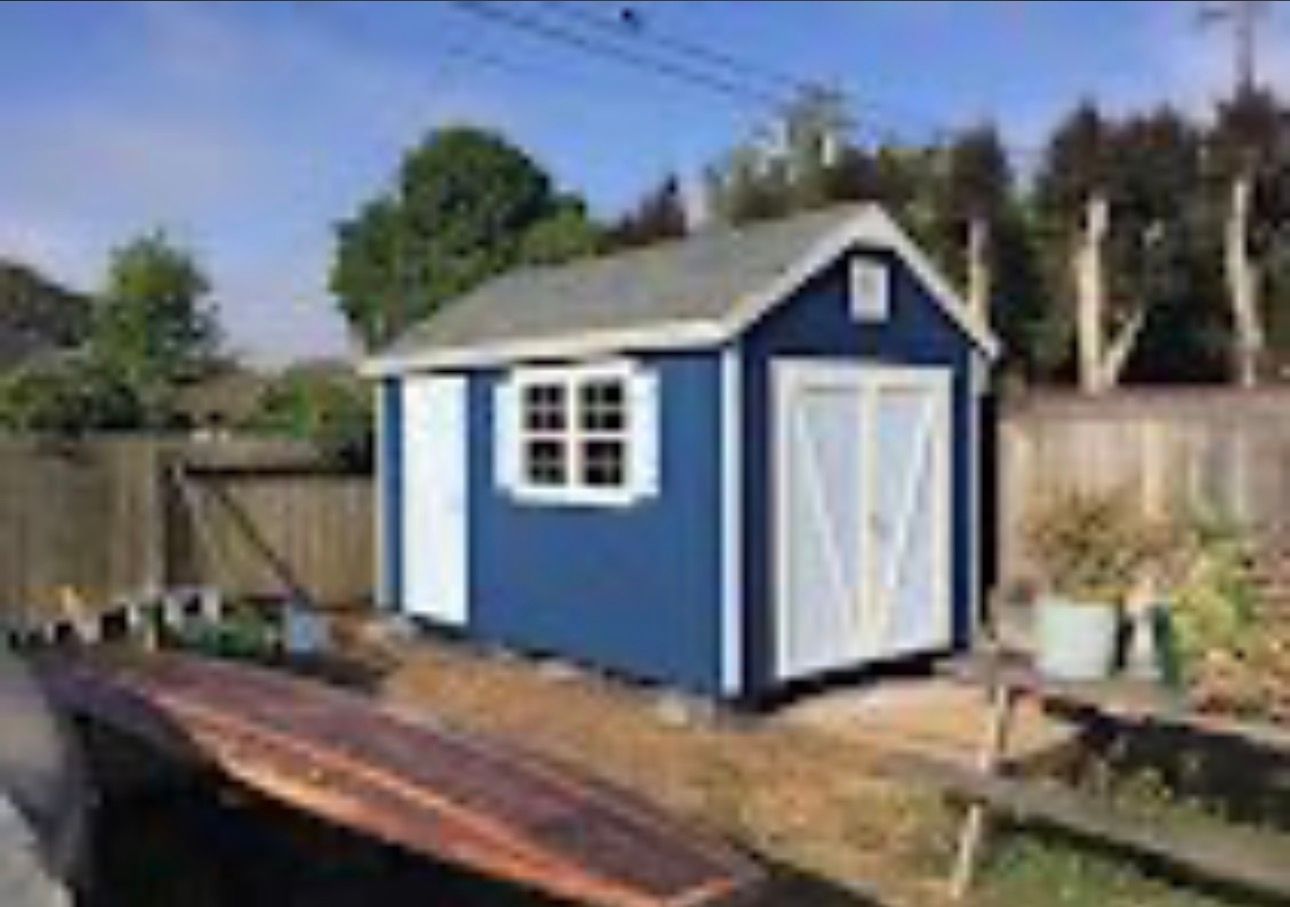 Blue backyard shed with white trim and double doors beside a fence and garden beds