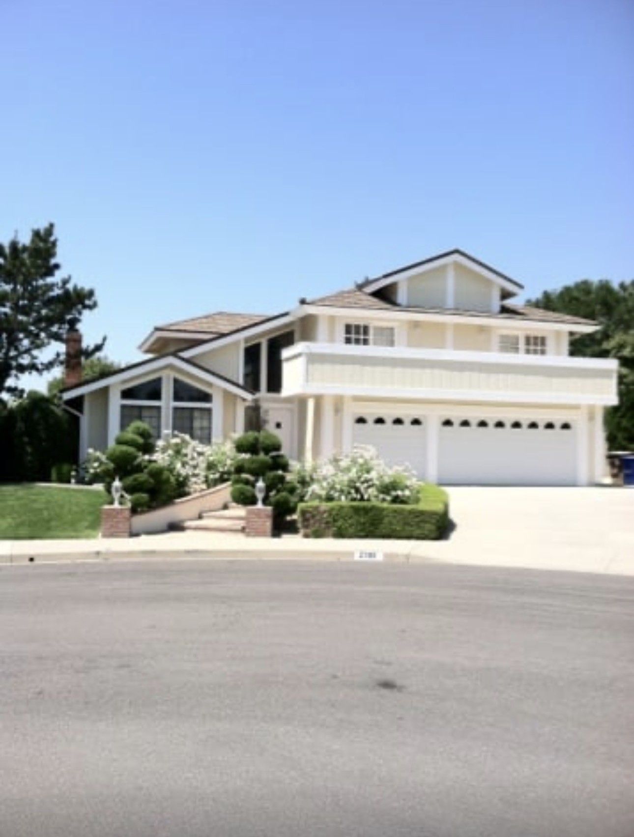 Suburban beige two-story house with white garage doors, front stairs, and a clear blue sky