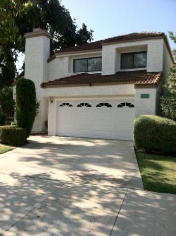 Two-story suburban house with white stucco exterior, double garage, and sunlit driveway