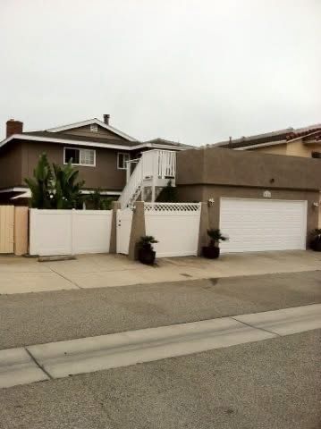 Suburban house with garage, white fence, and exterior stairs along a quiet street