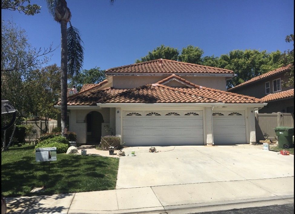 Two-story stucco house with terracotta roof and three-car garage under a clear blue sky