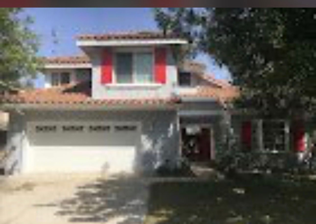 Two-story suburban house with white garage, red shutters, and trees in the front yard