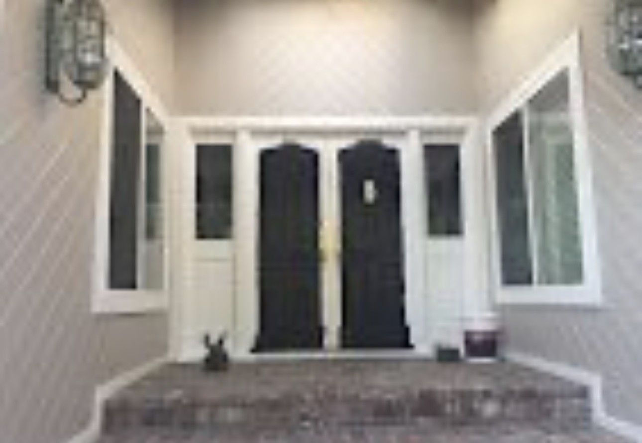Front porch with dark double front doors, white trim, brick steps, and potted plants on both sides.