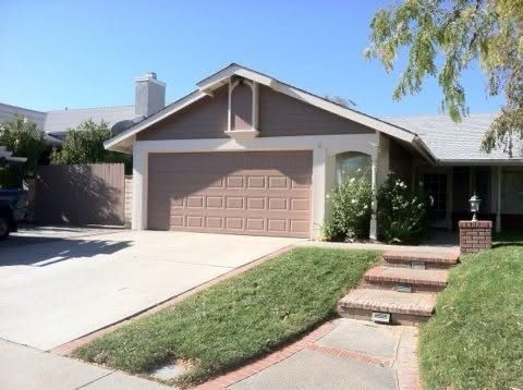 Suburban house with a tan garage, driveway, and front steps leading to the entry.