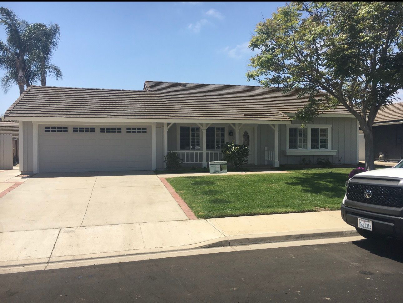 Suburban single-story house with a two-car garage, driveway, front lawn, and a parked SUV on the street